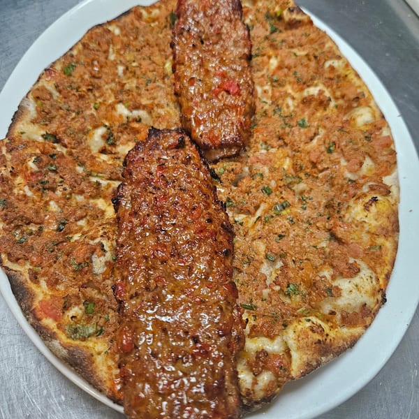 Two oval-shaped lahmacun flatbreads topped with minced meat and herbs, served with two grilled kebabs.