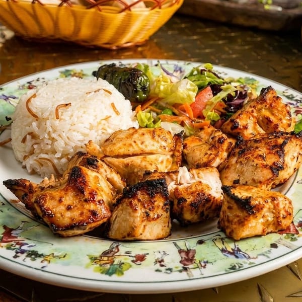 Grilled chicken shish tawook with rice, salad, and a glass of tea on a decorative plate.