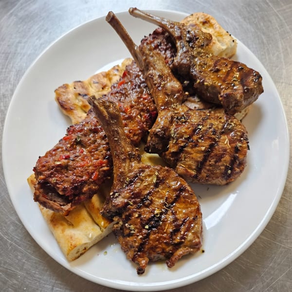 Grilled lamb chops and ground meat patties with spices, served on flatbread on a white plate.