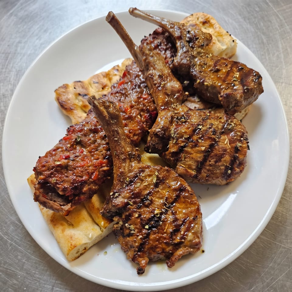 Grilled lamb chops and ground meat patties with spices, served on flatbread on a white plate.