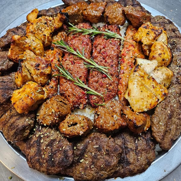A large platter of various grilled meats, including kebabs, chicken, and ground meat patties, garnished with rosemary.