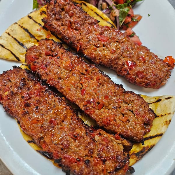 Three grilled Adana kebabs with red peppers on flatbread, served with a side salad.